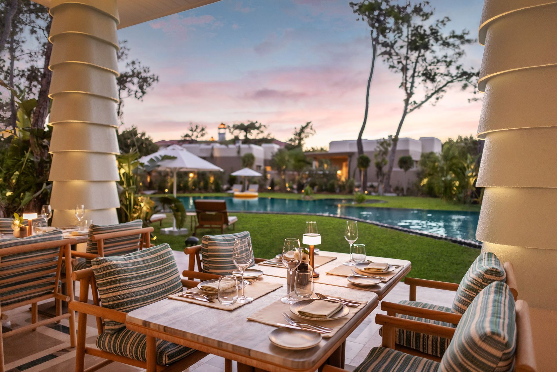 A patio with a table and chairs and a pool in the background.