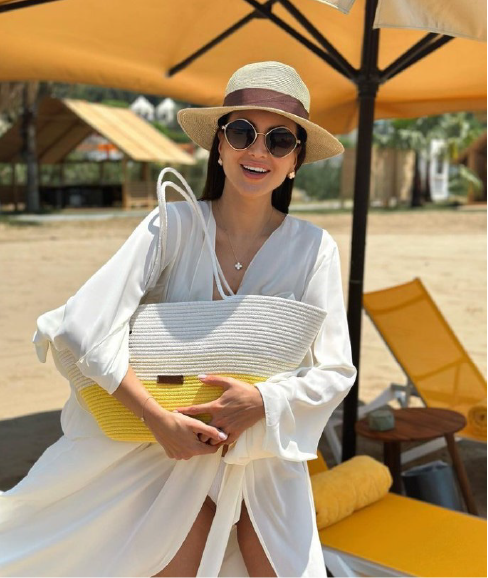 A woman wearing a hat and sunglasses is standing on a beach